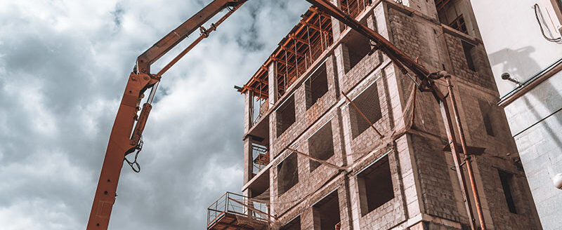 The top of concrete pump industrial machine with crane and tube to deliver concrete or cement mixture to the building under construction in the background, sunny summer day
